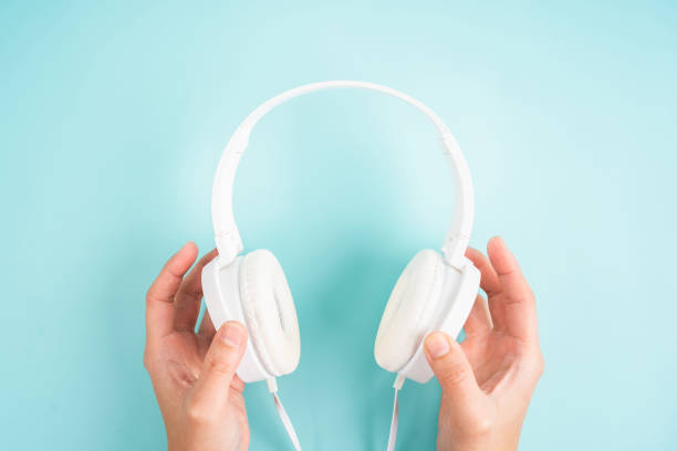 istock Female hands holding white headphones on blue background. 1342028979
