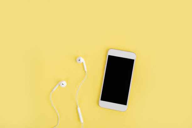 istock White headphones and mobile phone with blank screen on a yellow background top view. 1342028992