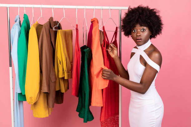 istock Puzzled Black Female Shopping Having Difficulties Choosing Clothes, Pink Background 1342029091