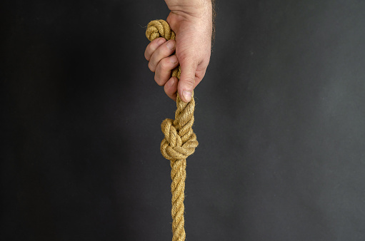 El macho adulto sostiene verticalmente una cuerda con un nudo. La mano sostiene un yel photo