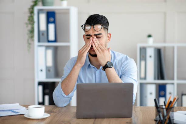 empleado árabe milenario frotándose los ojos cansados e irritados, trabajando demasiado con la computadora portátil, agotado del trabajo en línea en la oficina - financial burden fotografías e imágenes de stock