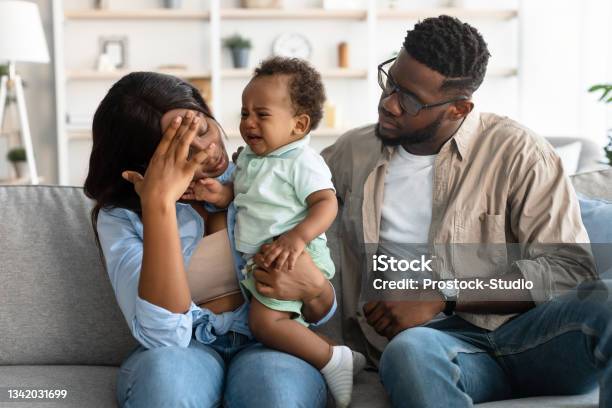 Tired African American Parents Sitting With Crying Kid On Sofa Stock Photo - Download Image Now