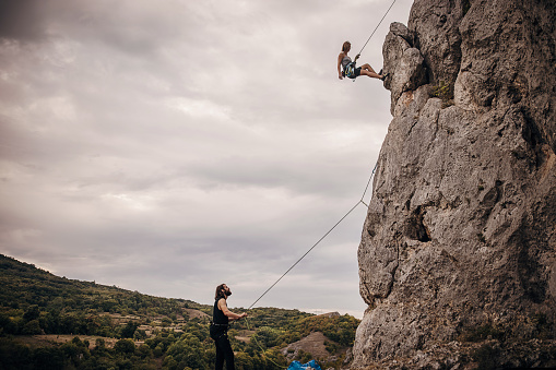 Young woman is trying to climb a rock while young man is holding safety harness