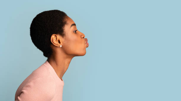 vista lateral de los labios de puchero de la joven mujer negra sobre el fondo azul del estudio - kissing blowing a kiss blowing women fotografías e imágenes de stock