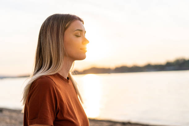 Young woman meditating on the riverside, enjoying the last sun rays of the day stock photo