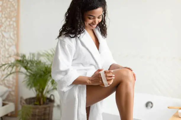 Happy African Female Making Massage With Dry Brush Massaging Hips And Legs Standing In Modern Bathroom At Home. Cellulite Prevention And Bodycare Concept. Cropped