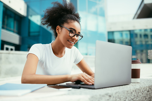 Chica universitaria afroamericana usando computadora portátil aprendiendo en línea al aire libre photo