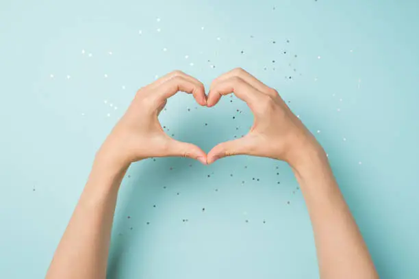 Photo of First person top view photo of female hands making heart with fingers on isolated pastel blue background with copyspace