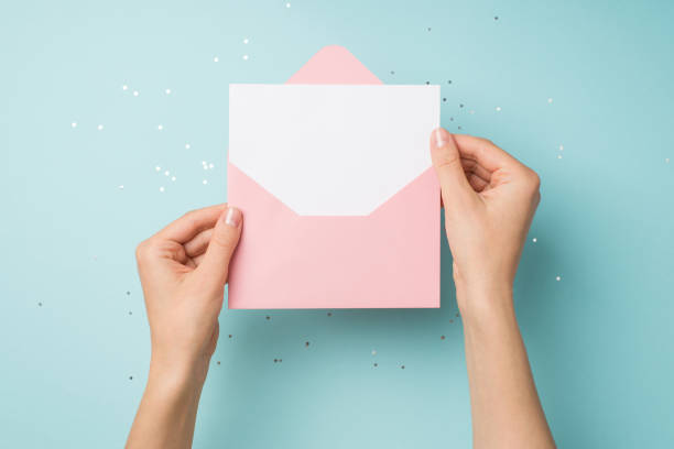 First person top view photo of hands holding open light pink envelope with white card over shiny sequins on isolated pastel blue background with blank space First person top view photo of hands holding open light pink envelope with white card over shiny sequins on isolated pastel blue background with blank space pink envelope stock pictures, royalty-free photos & images