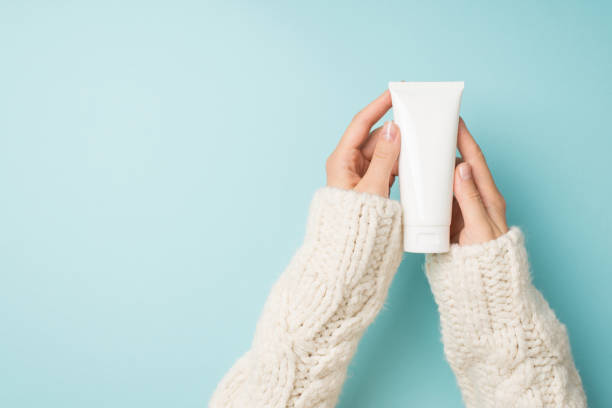 first person top view photo of female hands in white sweater holding white cream tube without label on isolated pastel blue background with blank space - moisturizer cosmetics merchandise human hand imagens e fotografias de stock