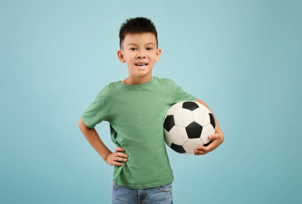 glücklicher kleiner asiatischer junge mit fußball in der hand über blauem hintergrund - soccer child indoors little boys stock-fotos und bilder
