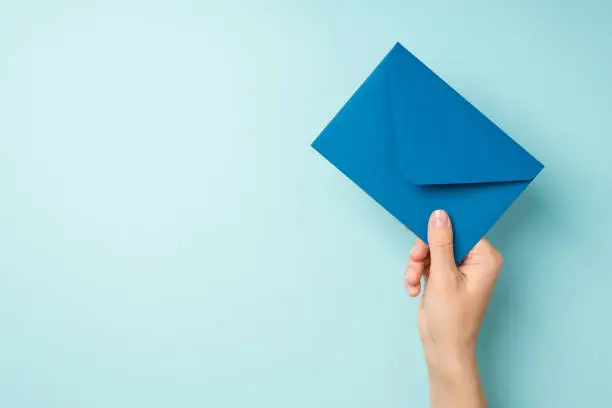 Photo of First person top view photo of hand holding closed blue envelope on isolated pastel blue background with copyspace
