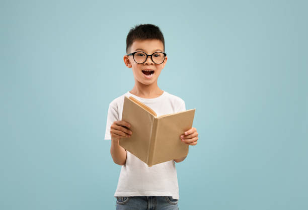 istock Excited little asian boy wearing eyeglasses holding and reading open book 1342037809