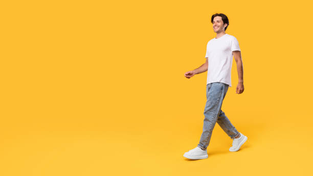 Young bearded man walking isolated on yellow background Advertising And Marketing. Full length body size profile side view of nice cheerful bearded guy in casual white t-shirt and jeans walking looking at free empty space isolated over orange color wall urbane stock pictures, royalty-free photos & images