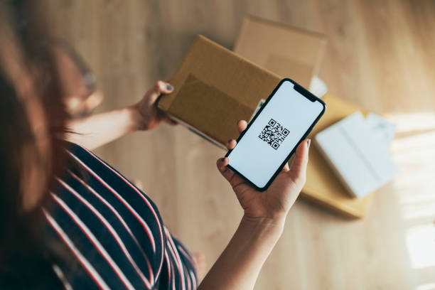 Asian woman scanning QR code of parcel young Asian woman checking smartphone while receiving a parcel at home scanning activity stock pictures, royalty-free photos & images