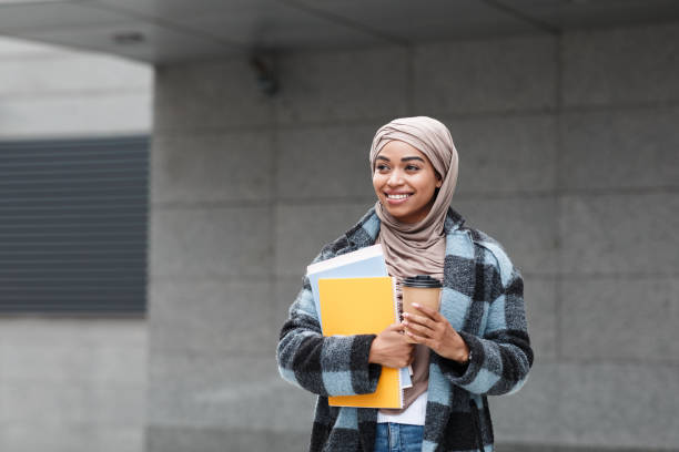 Happy pretty cute afro american female student in hijab and coat with books and cup of coffee ready to study Happy pretty cute afro american female student in hijab and coat with books and cup of coffee ready to study, empty space. Modern education, knowledge, learn and new normal after covid-19 quarantine pics of a cute muslim outfits stock pictures, royalty-free photos & images