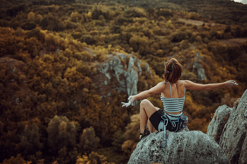 Young woman rock climber sitting on the top of the cliff