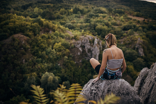 Young woman rock climber sitting on the top of the cliff