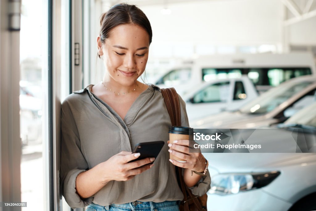 Shot of a young woman using her smartphone to send text messages This decision is so nerve wracking Car Stock Photo