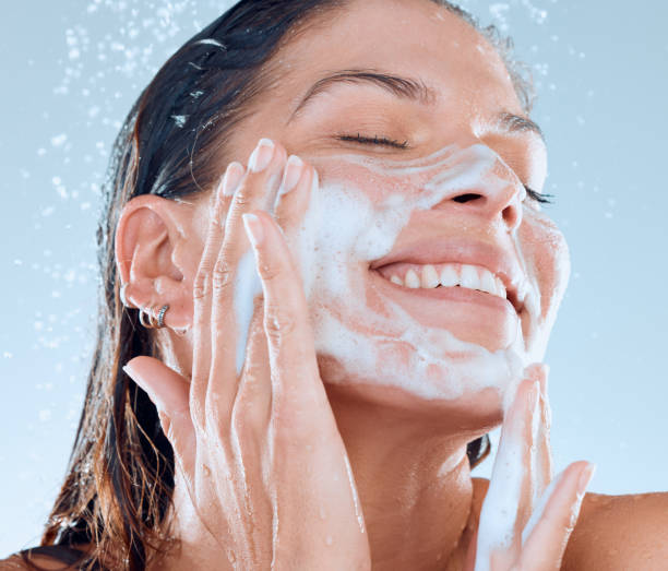 青い背景にシャワーを浴びている間、彼女の顔を洗う若い女性のスタジオショット - human face water washing women ストックフォトと画像