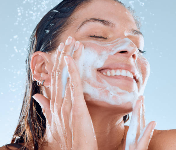 studio shot of a young woman washing her face while taking a shower against a blue background - facial cleanser imagens e fotografias de stock