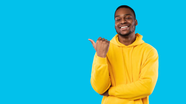 istock Smiling African Guy Pointing Thumb Finger Aside Over Blue Background 1342041450