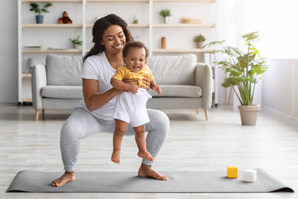 Weight Loss After Pregnancy. Black Mom Training At Home With Infant Baby Weight Loss After Pregnancy. Happy Black Mom Training At Home With Infant Baby, Making Squats While Holding Her Cute Toddler Son In Hands, Exercising Pilates On Fitness Mat In Living Room, Copy Space baby squatting stock pictures, royalty-free photos & images