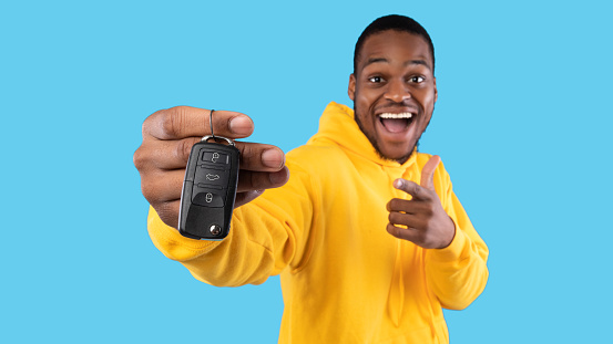 New Car. Excited Black Man Showing Key In Excitement Celebrating Buying New Auto Posing Standing On Blue Studio Background. Dreams Come True, Own Automobile Concept. Panorama, Selective Focus