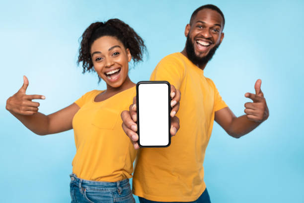 istock Excited Afro couple pointing at cellphone with blank screen, recommending new app on blue background, mockup for website 1342042377