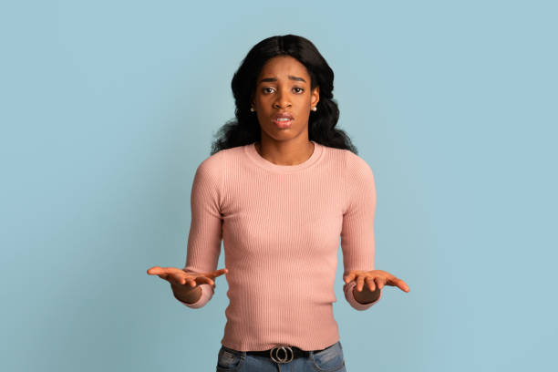 i don't know. unsure young black female shrugging shoulders and spreading arms - blank expression head and shoulders horizontal studio shot imagens e fotografias de stock
