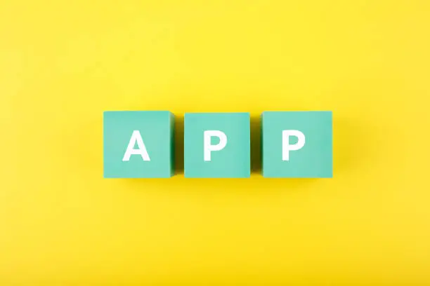 Photo of App written on blue cubes against bright yellow background