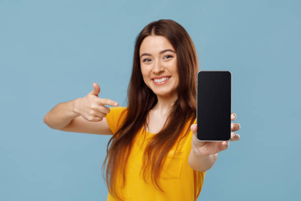 istock Cheerful beautiful lady pointing at smartphone with blank screen, mockup 1342043820