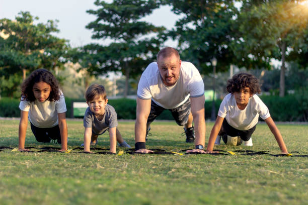 портрет трех счастливых улыбающихся детей и их тренера, делающего упражнения на отжимания - yoga challenge for 3 стоковые фото и изображения