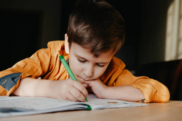 istock Cute 7 years old child doing his homework sitting by desk 1342048301