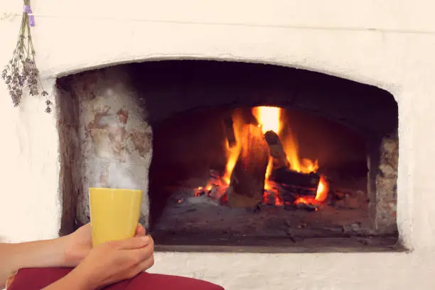 yellow mug in hands against the background of the stove with burning wood