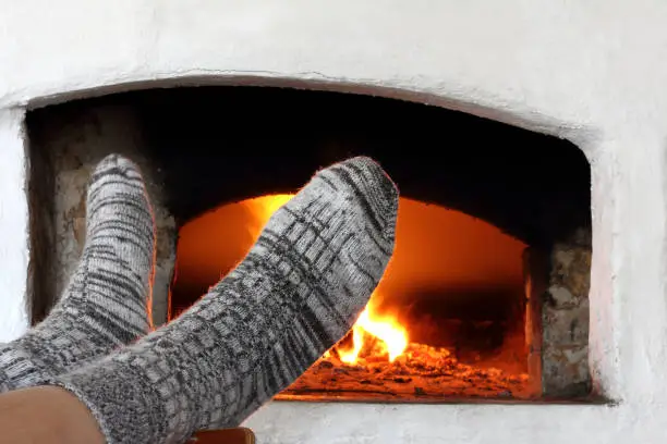 gray knitted socks are worn on the legs against the background of the stove with burning wood