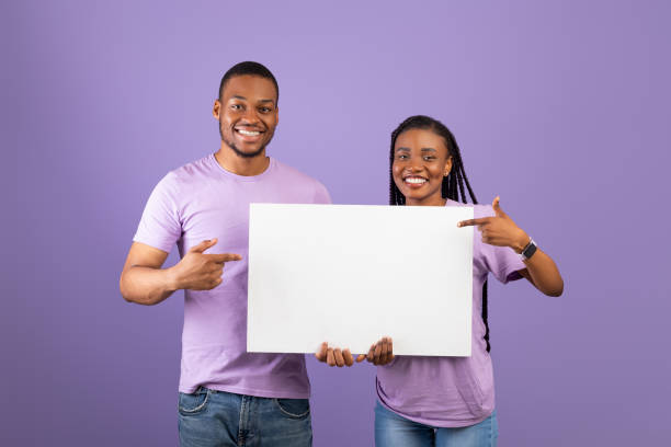 istock Black couple holding and pointing at blank white advertising placard 1342050146