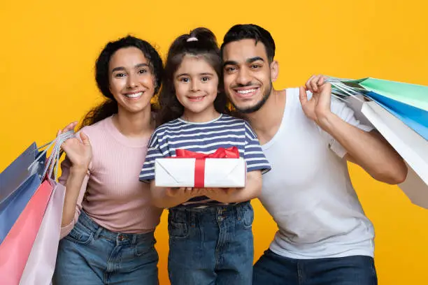 Photo of Portrait of happy middle-eastern family of three holding shopping bags and gift