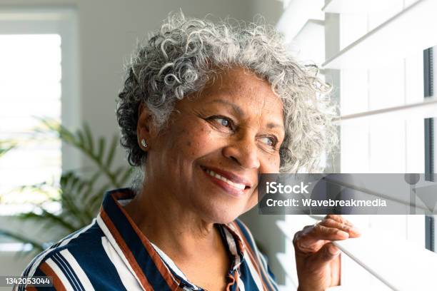 Portrait Of Smiling African American Senior Woman Looking Through Window Stock Photo - Download Image Now