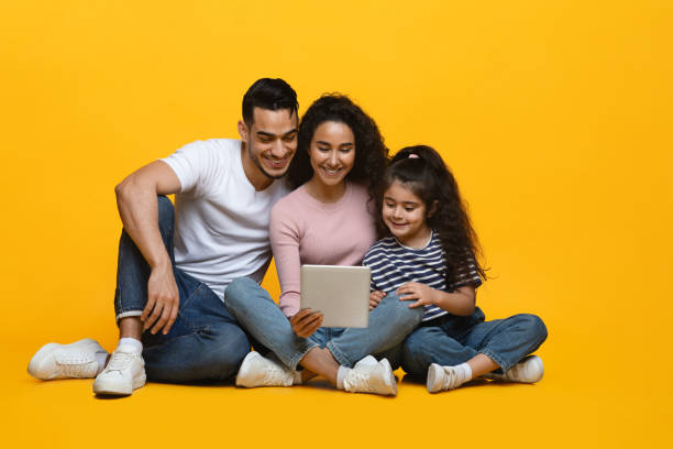 istock Happy Middle-Eastern Family Of Three With Digital Tablet On Yellow Studio Background 1342053186
