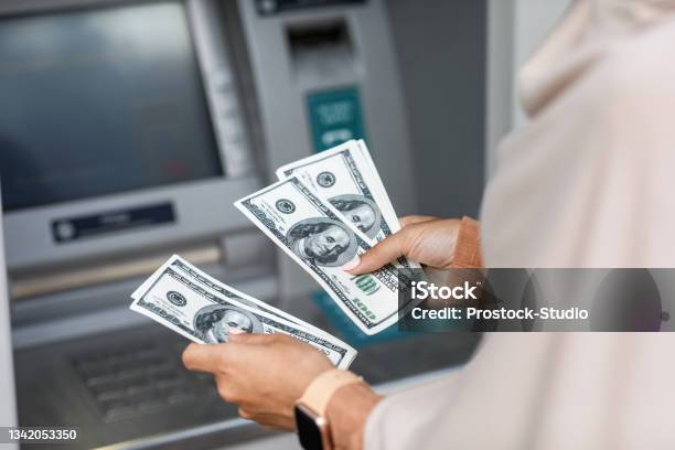 Hands Of Unrecognizable Young Arabian Business Woman In Hijab Counts Dollars Near Atm With Empty Screen Stock Photo - Download Image Now