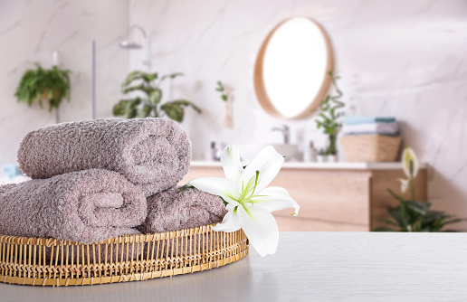 Fresh towels and lily flower on wooden table in bathroom. Space for text