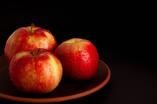 Close up of red yellow apples with water drops on the dark brown plate on black background. Healthy organic food, autumn mood and still life low key concept with copy space.