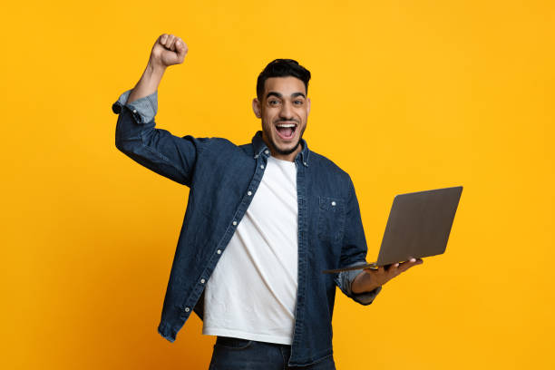 istock Emotional arab guy with new modern laptop on yellow 1342055522