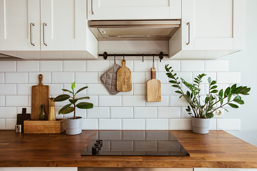 Utensilios de latón de cocina, accesorios de chef. Cocina colgante con pared de azulejos blancos y mesa de madera. Planta verde en el fondo de la cocina photo