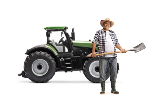 Full length portrait of a mature farmer with a shovel in front of a green tractor isolated on white background