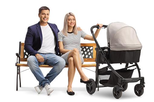 Full length portrait of a young couple sitting on a bench with a pushchair isolated on white background