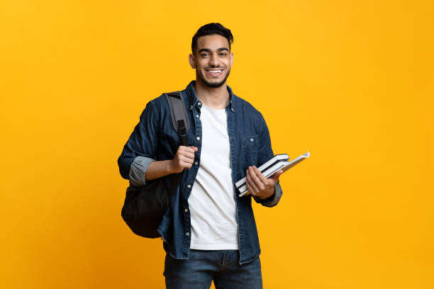 Smart arab guy student with backpack and books Smart arab guy student with backpack and bunch of books smiling at camera, copy space for advertisement over yellow studio background. Education, university, college, studying, course concept university students stock pictures, royalty-free photos & images