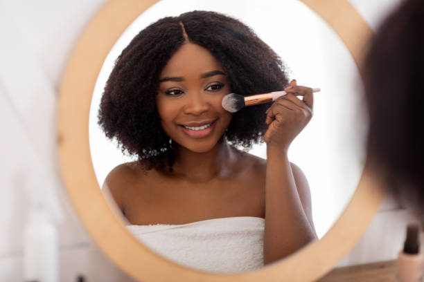 istock Pretty black lady applying makeup near mirror, using decorative cosmetics indoors 1342062291