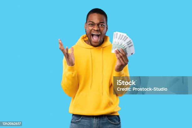 Emotional Black Man Shouting Holding Euro Money Over Blue Background Stock Photo - Download Image Now